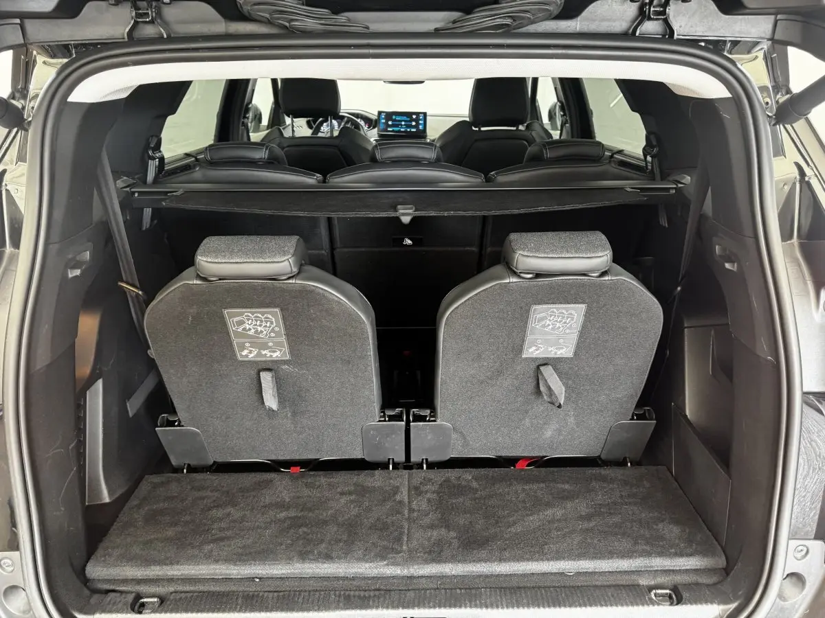 Vue arrière du coffre ouvert d’un Peugeot 5008 noir 2022, montrant la 3ème rangée de sièges individuels rabattus.