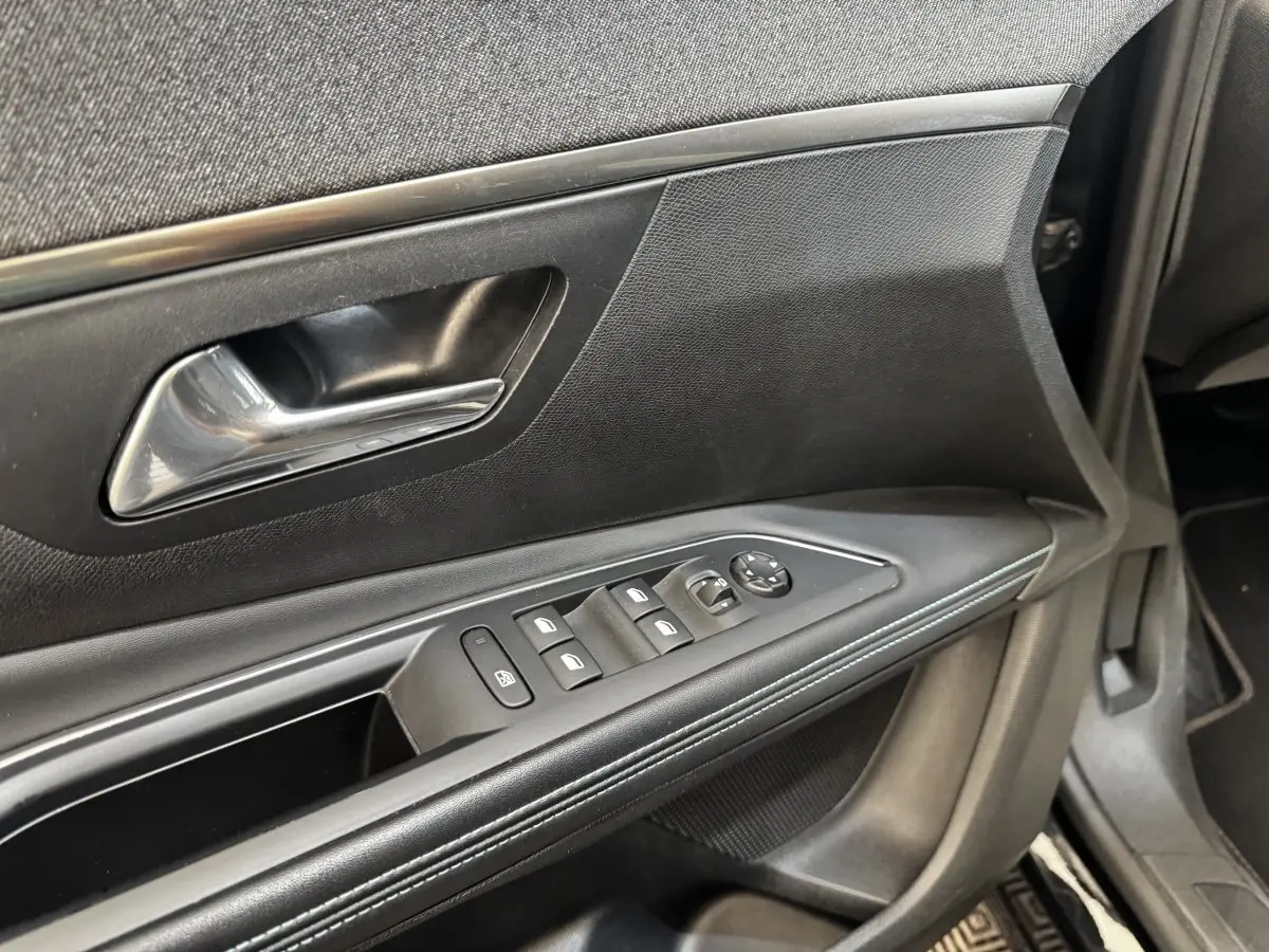 Gros plan sur la porte intérieure côté conducteur du Peugeot 5008 noir, avec commandes des vitres et poignée chromée.