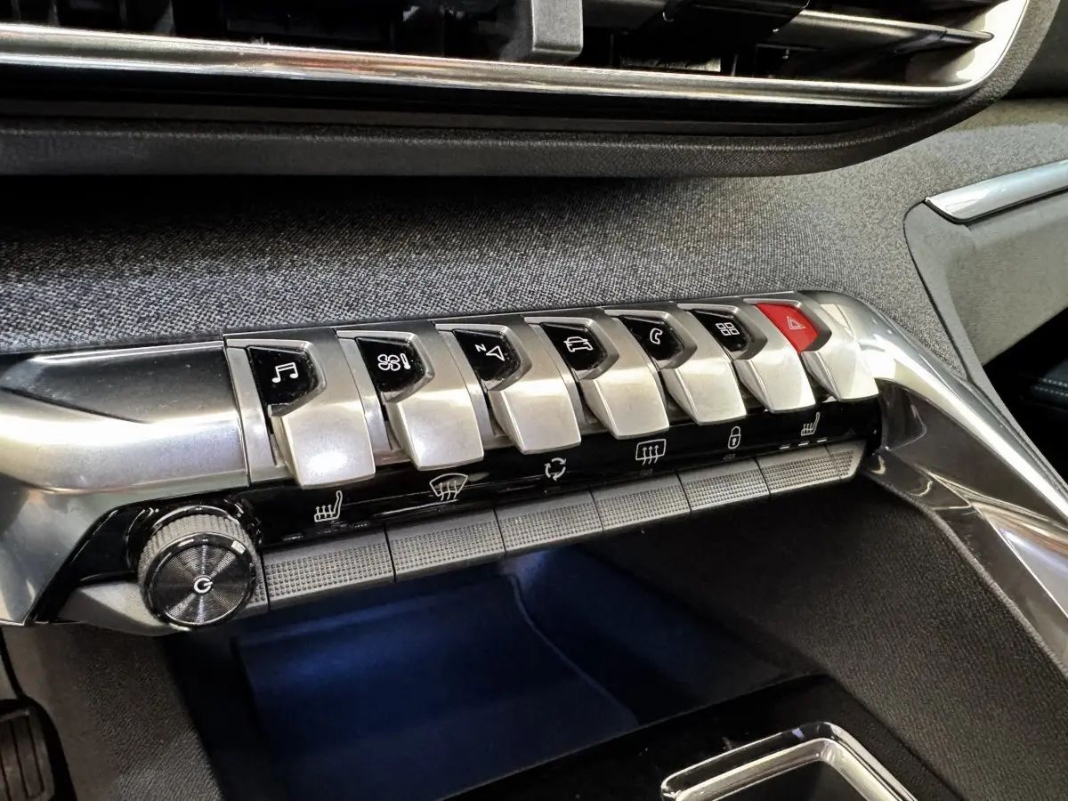 Gros plan sur la rangée de boutons argentés du tableau de bord du Peugeot 5008 noir, avec finition tissu gris.