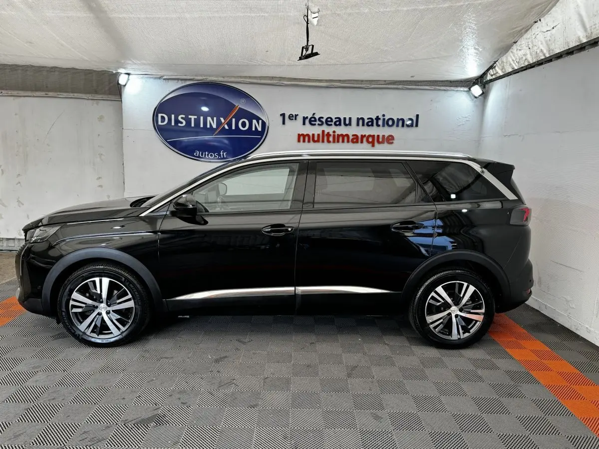 Profil latéral droit d'un Peugeot 5008 noir 2022 avec jantes alliage et barres de toit chromées, en intérieur showroom.