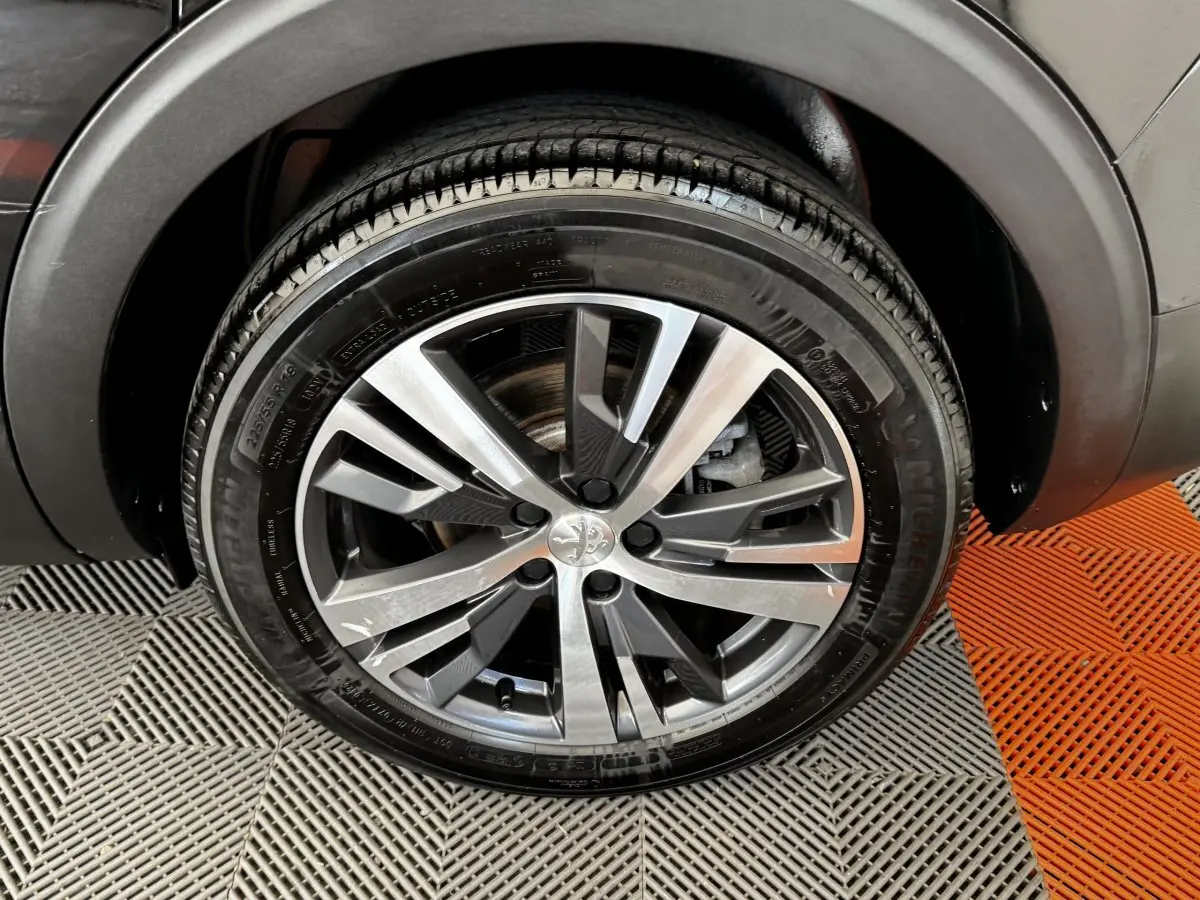Gros plan sur la roue avant droite du Peugeot 5008 noir, mettant en valeur la jante alliage moderne et le pneu Michelin.