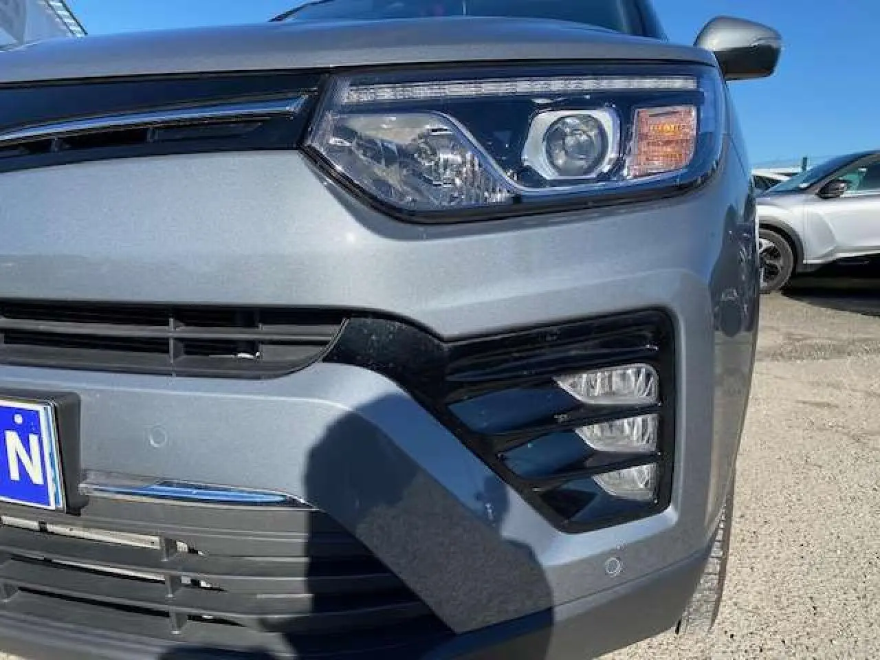 Gros plan sur l'avant droit du SsangYong Tivoli gris foncé 2021, mettant en valeur son phare et sa calandre noire.