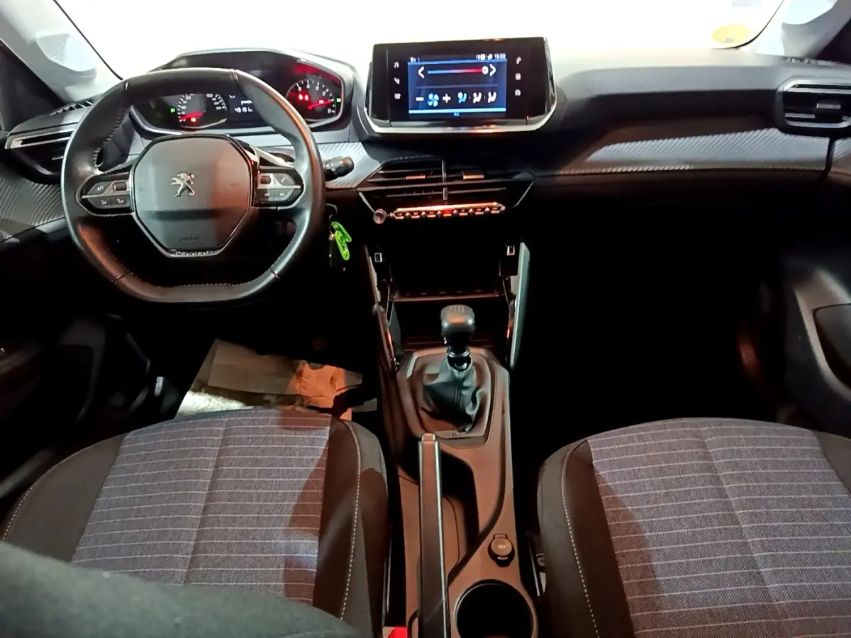 Vue intérieure avant de la Peugeot 208 1.5 BlueHDi 100 S&S Premium, montrant le volant compact, la console centrale avec boîte manuelle et l’écran tactile.