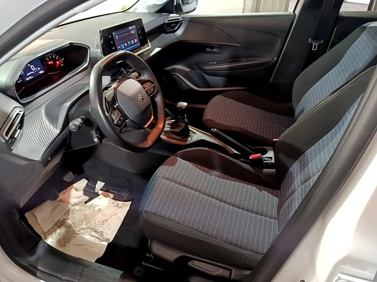Vue intérieure côté conducteur de la Peugeot 208 1.5 BlueHDi 100 S&S Premium, montrant sièges tissu gris et tableau de bord moderne.