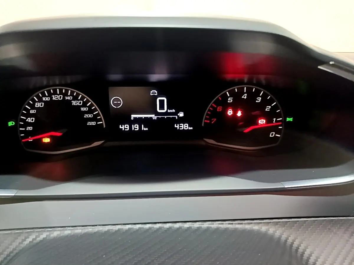 Vue rapprochée du tableau de bord numérique de la Peugeot 208 blanc, affichant la vitesse à 0 km/h et le compteur kilométrique.