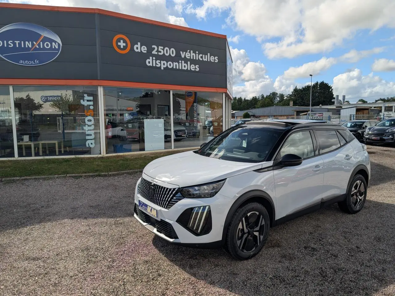 Peugeot 2008 blanc vue 3/4 avant droit avec toit noir et jantes alliage bi-ton devant un concessionnaire.