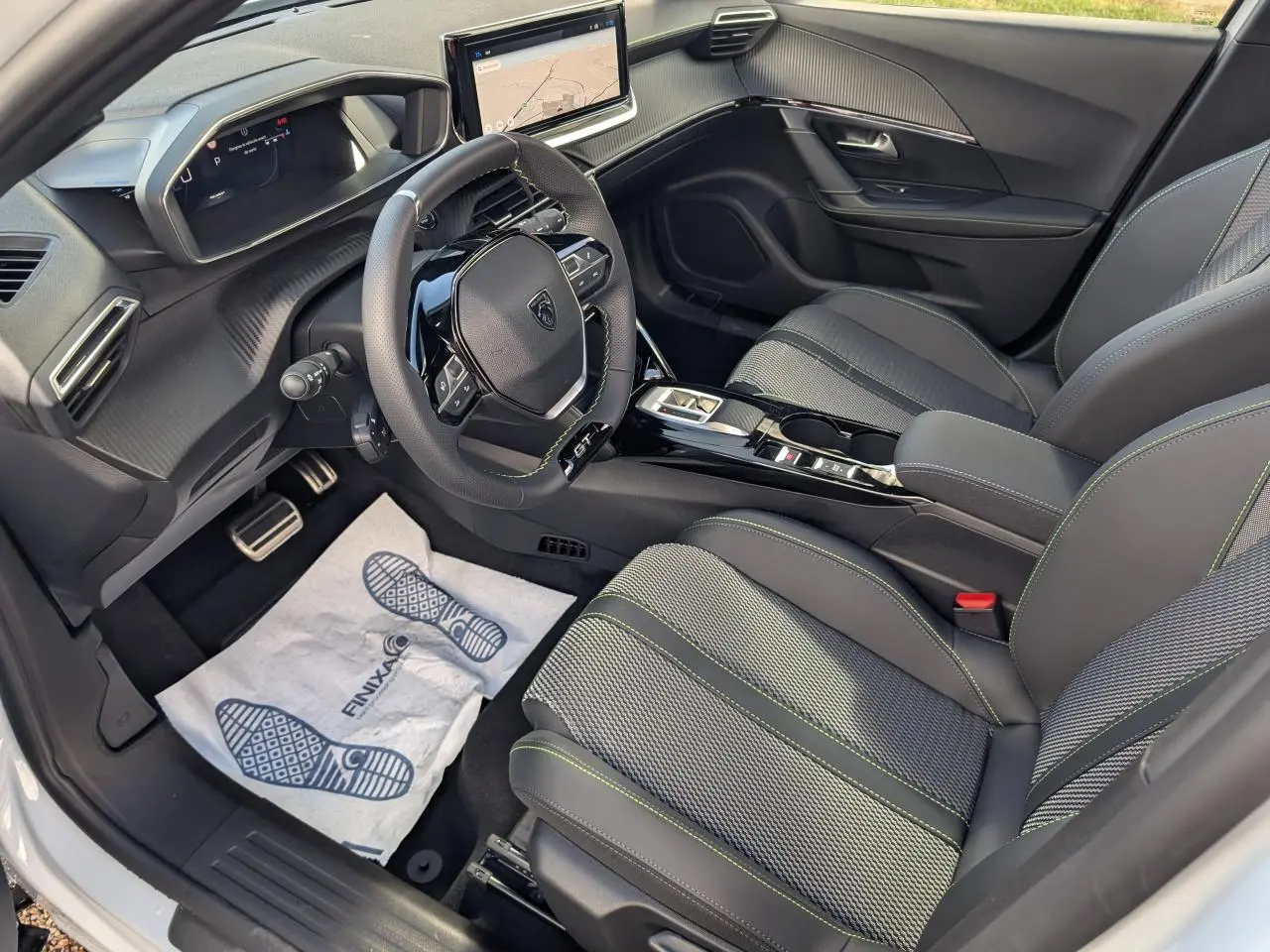 Vue intérieure côté conducteur du Peugeot 2008 GT 2026, sièges tissu gris avec surpiqûres vertes et volant compact cuir noir.