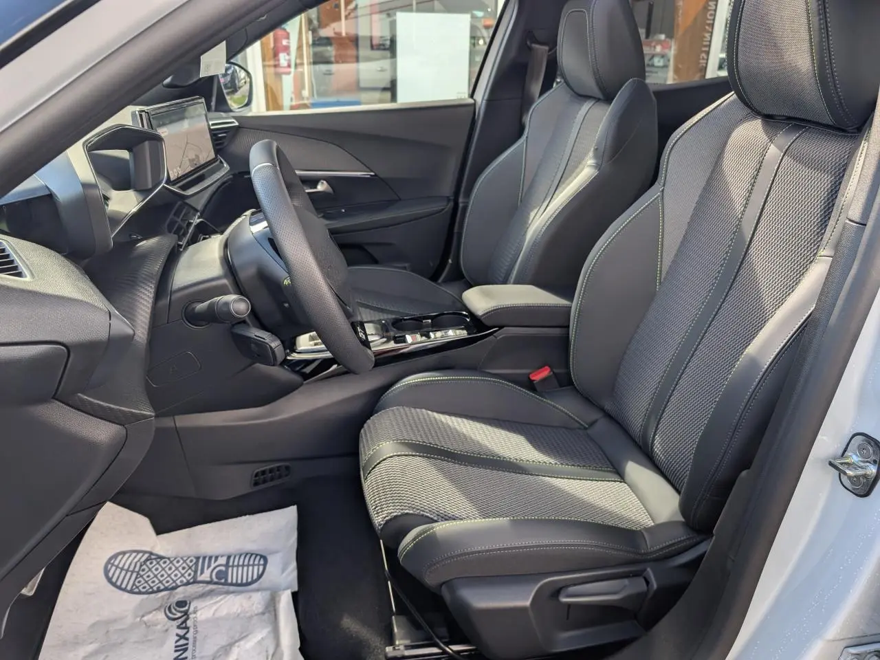 Vue intérieure côté conducteur du Peugeot 2008 blanc 2026, sièges sport gris avec surpiqûres vertes et tableau de bord moderne.
