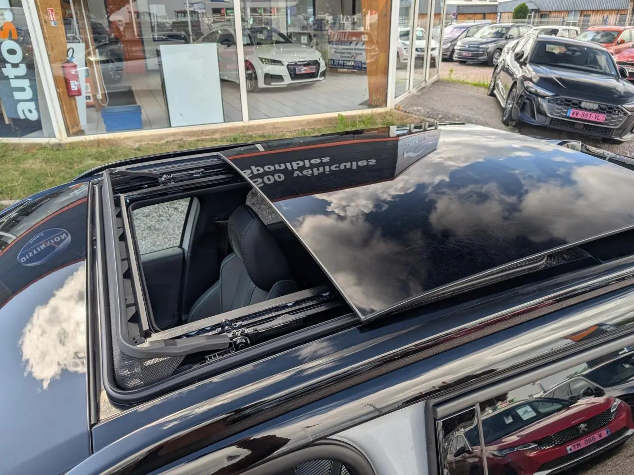 Vue en plongée sur le toit ouvrant noir ouvert d'une Peugeot 2008 blanche, avec intérieur visible côté gauche.