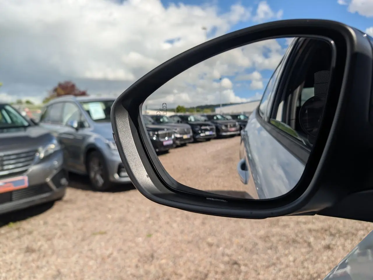 Rétroviseur droit d'une Peugeot 2008 blanche GT hybride, avec vue sur plusieurs véhicules en arrière-plan.