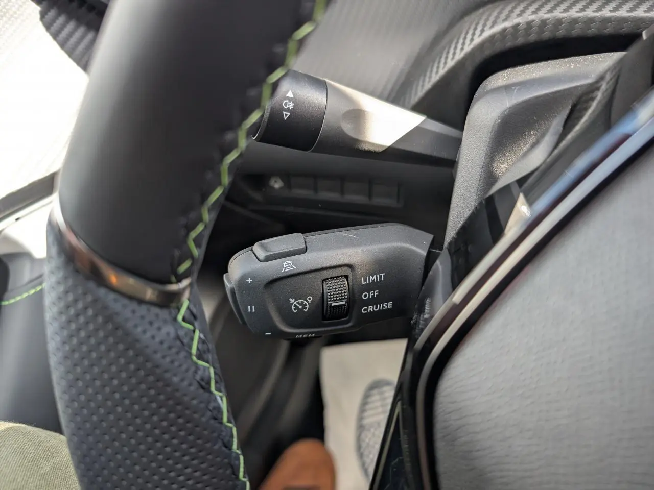Gros plan sur la commande de régulateur de vitesse au volant cuir noir avec surpiqûres vertes du Peugeot 2008 blanc.