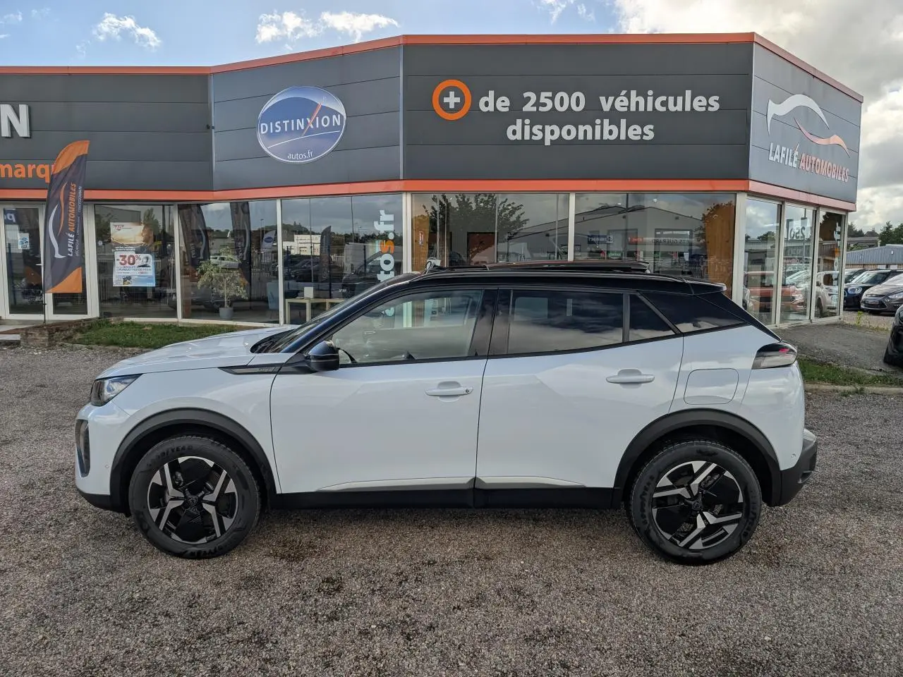 Profil droit d’un Peugeot 2008 blanc avec toit noir et jantes alliage 17'' bi-ton, stationné devant un concessionnaire.