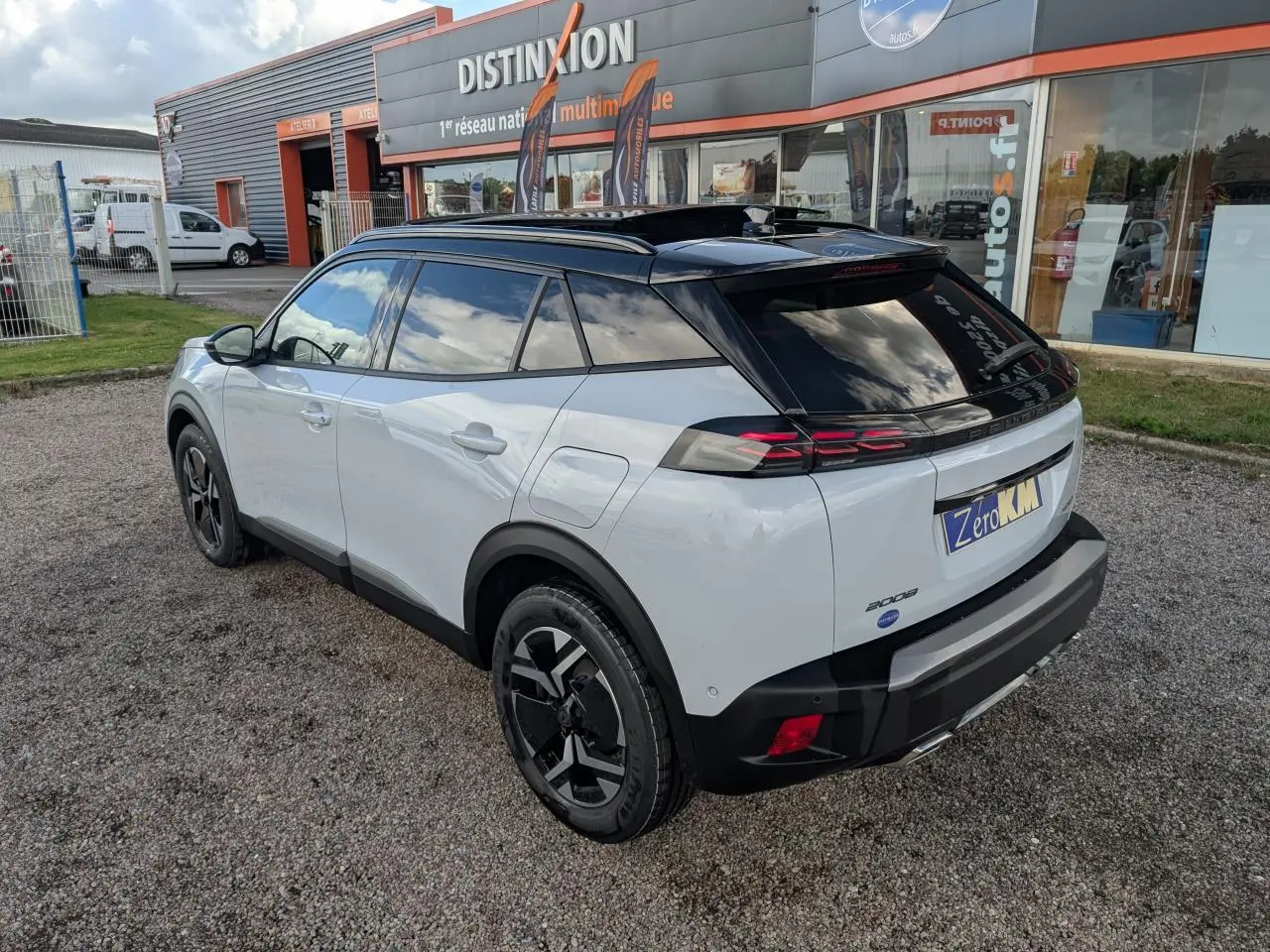 Vue 3/4 arrière droite d’un Peugeot 2008 blanc avec toit noir et jantes alliage bi-ton, stationné devant un magasin.