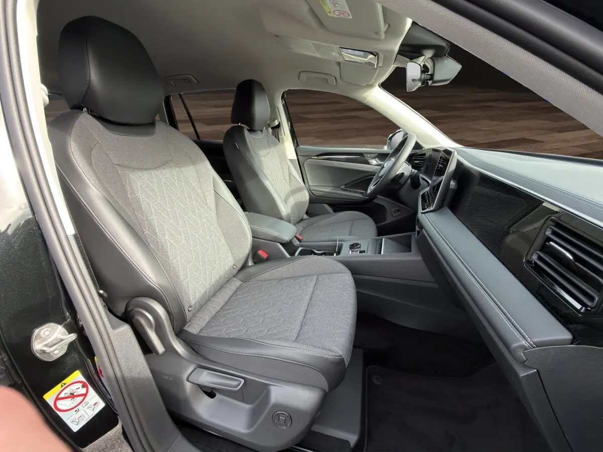 Vue intérieure côté conducteur du Volkswagen Tiguan noir 2026, sièges tissu gris avec accoudoirs et tableau de bord moderne.