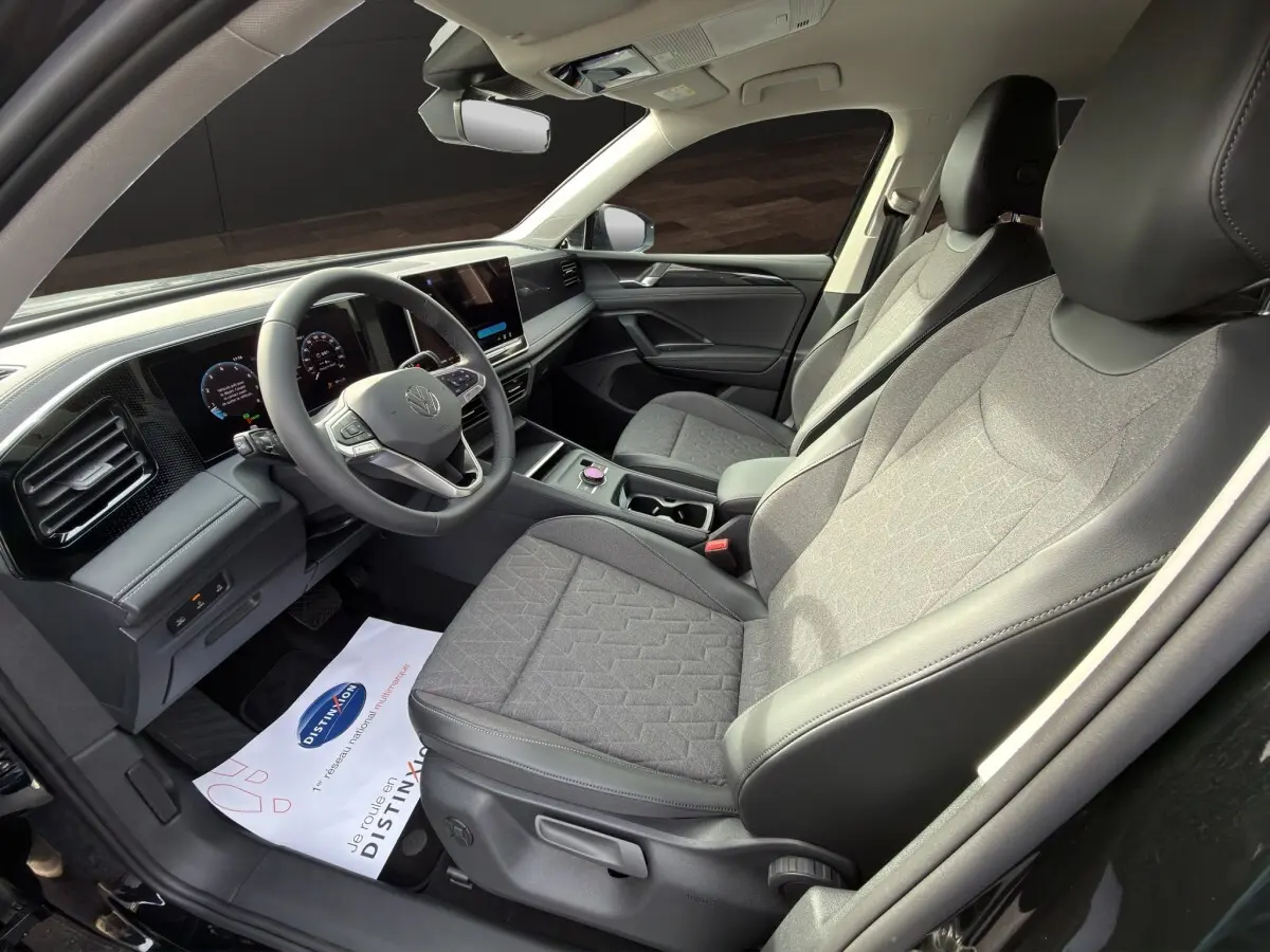 Vue intérieure côté conducteur du Volkswagen Tiguan 2026 noir, montrant sièges tissu gris et tableau de bord digital.