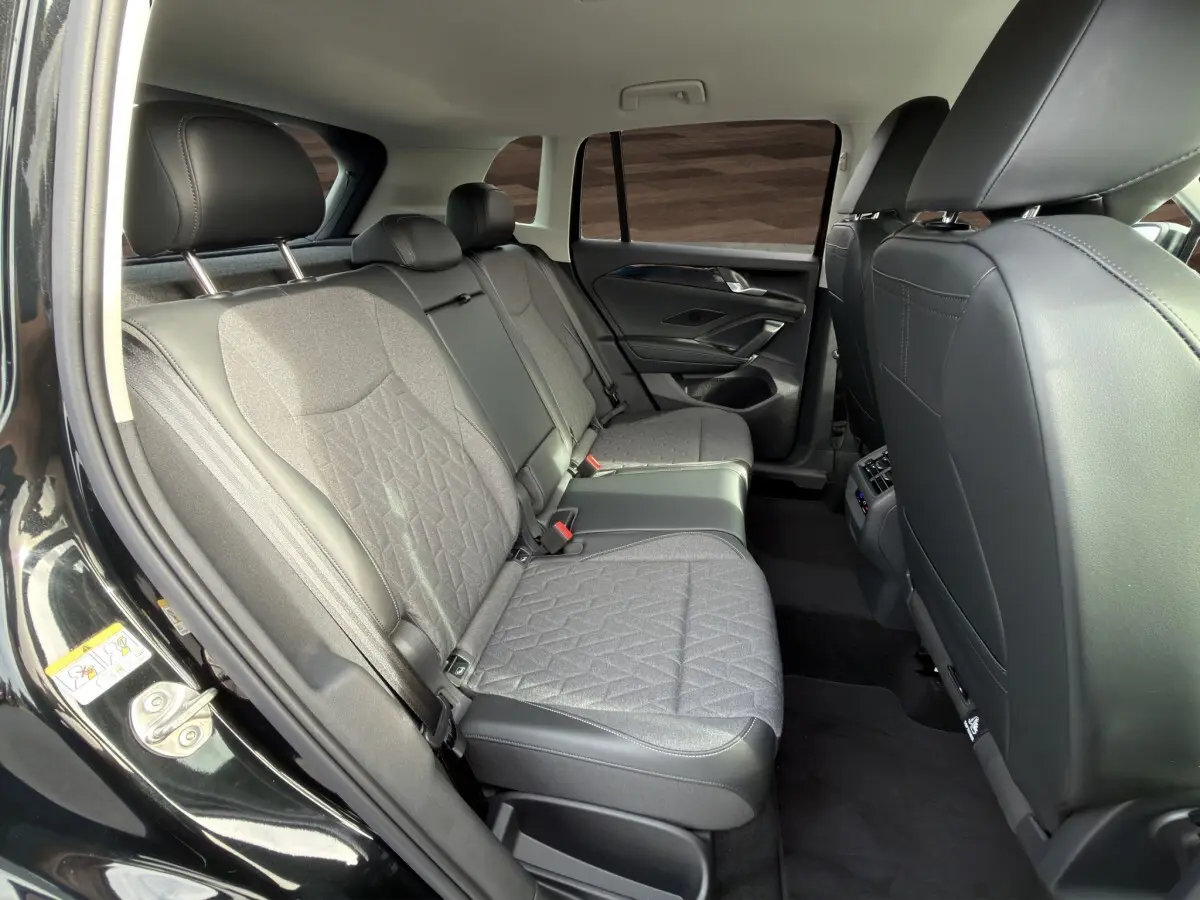 Vue intérieure arrière côté gauche du Volkswagen Tiguan 2026 noir, montrant la banquette tissu et cuir gris avec accoudoir central.