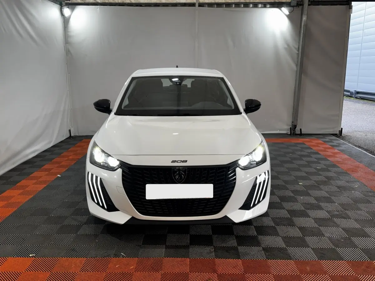 Vue de face d'une Peugeot 208 blanche 2024 avec phares LED allumés et calandre noire distinctive.