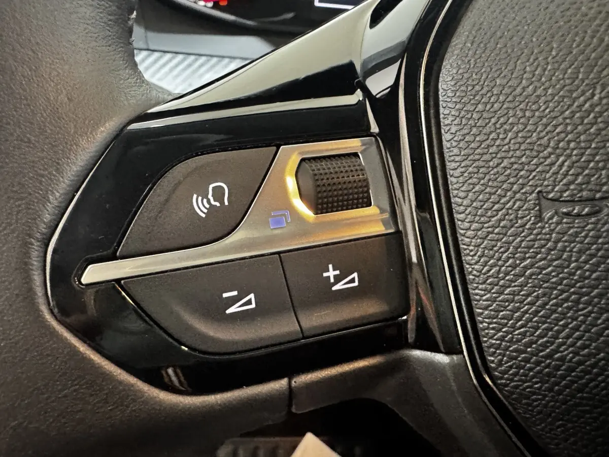 Gros plan sur les commandes vocales et volume au volant cuir noir de la Peugeot 208 PureTech 75 S&S Active.