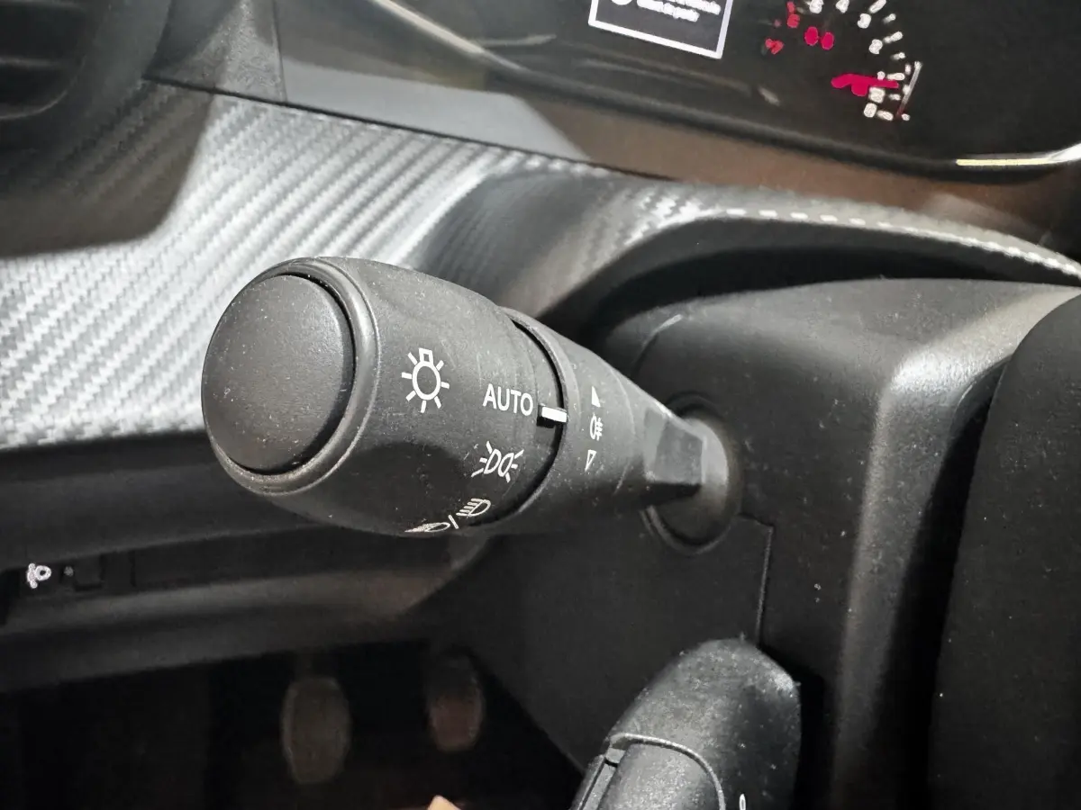 Gros plan sur la commande des phares à gauche du volant dans l’habitacle d’une Peugeot 208 blanche 2024.