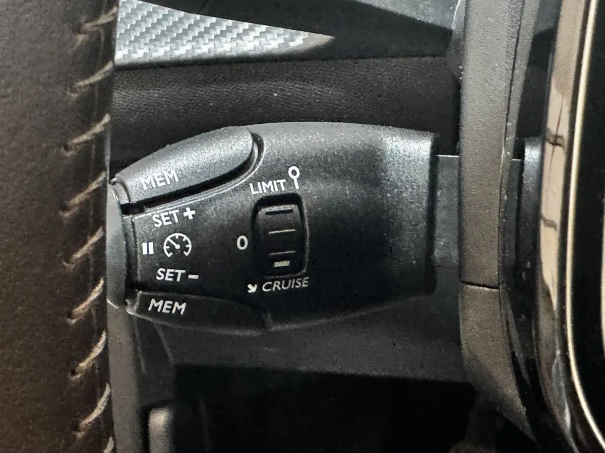 Gros plan sur la commande de régulateur de vitesse noire à gauche du volant dans l’habitacle d’une Peugeot 208 blanche 2024.
