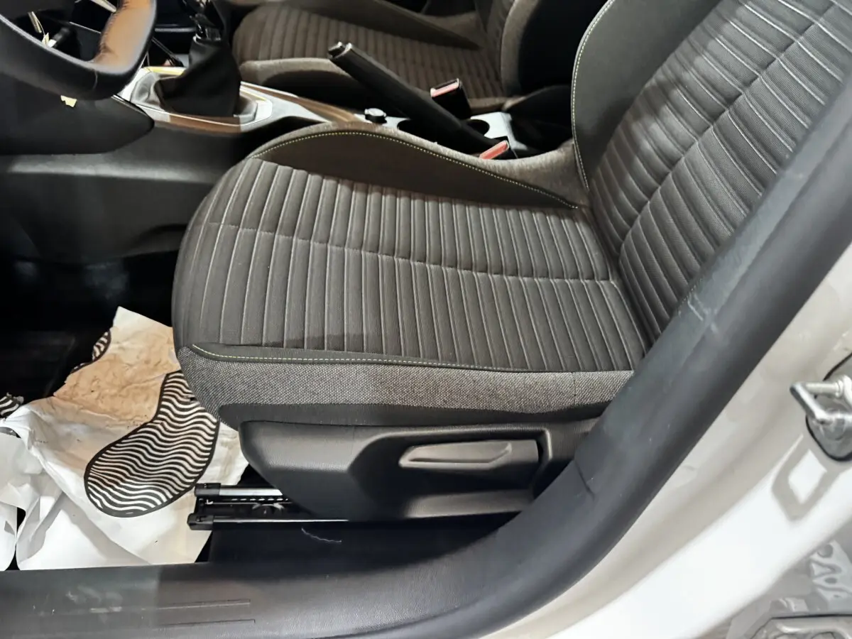 Vue rapprochée du siège avant droit gris à coutures vertes dans l’habitacle d’une Peugeot 208 blanche.