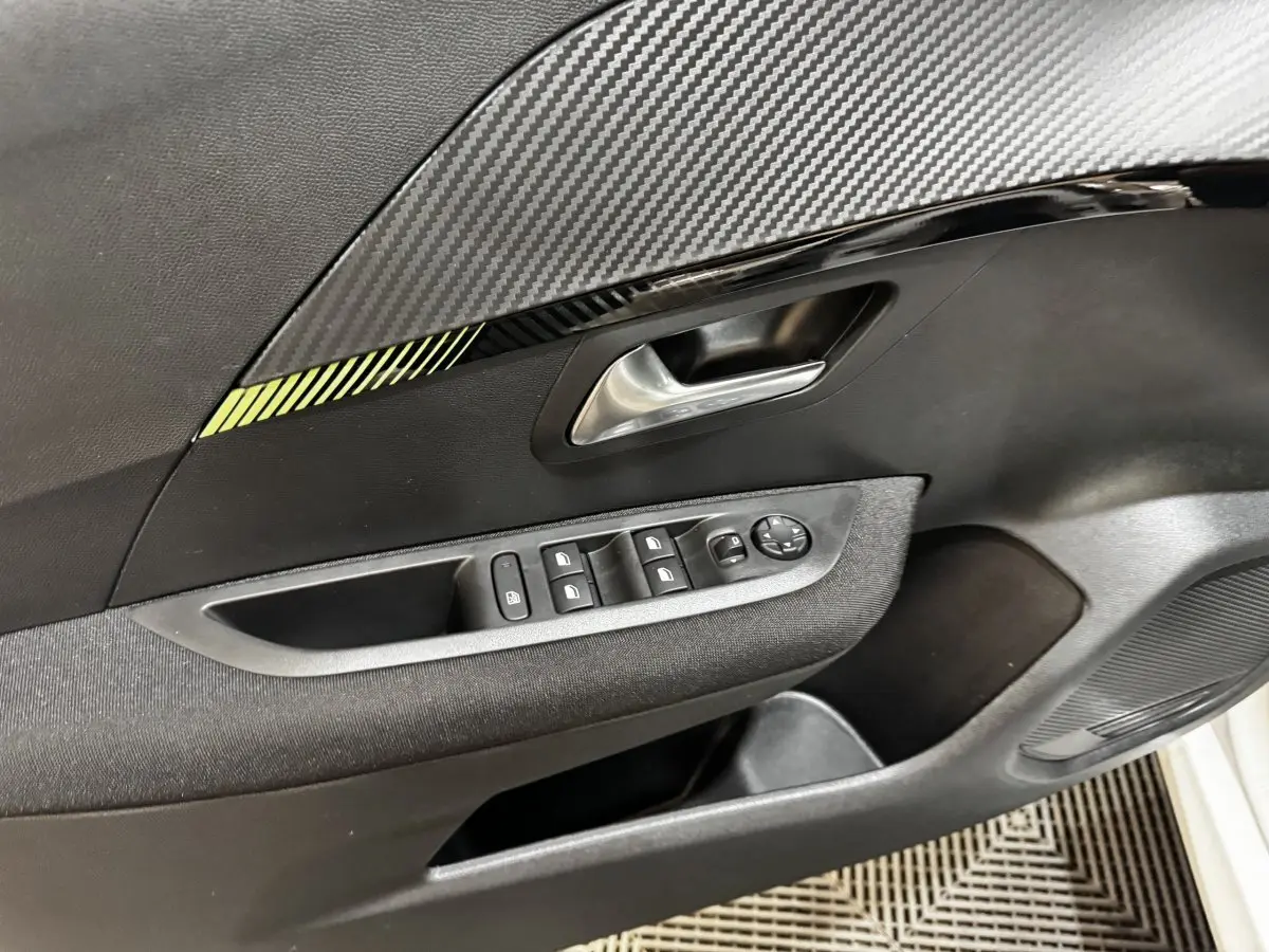 Détail de la porte intérieure côté gauche de la Peugeot 208 PureTech 75 S&S Active avec commandes de vitres et décor carbone.