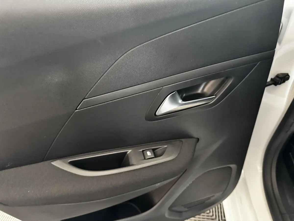 Vue rapprochée de la porte avant droite noire d’une Peugeot 208 blanche, avec poignée et commande de vitre.