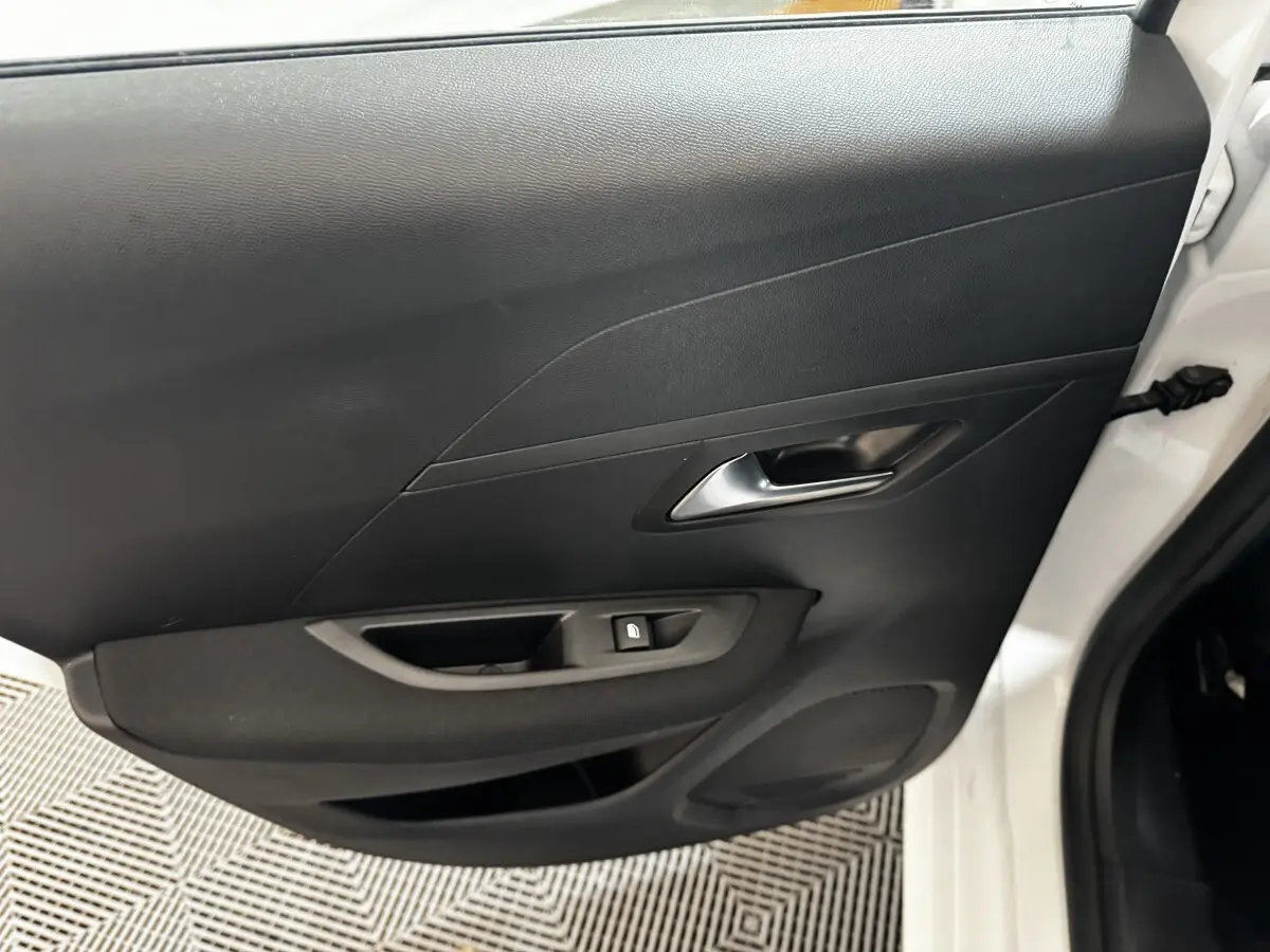 Vue rapprochée de la porte arrière droite noire d'une Peugeot 208 blanche, avec poignée et commande de vitre.