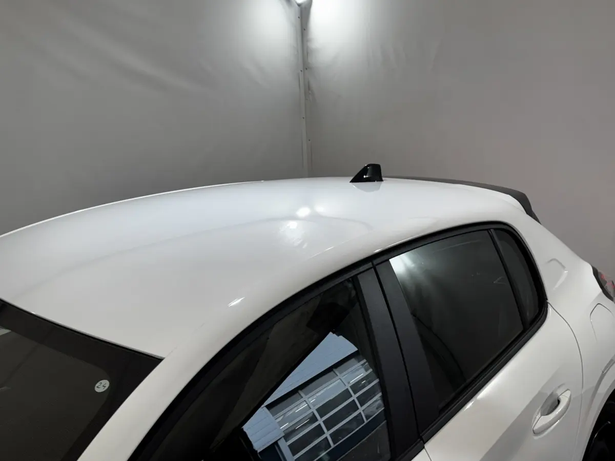 Vue 3/4 arrière droite d'une Peugeot 208 blanche 2024 avec toit lisse et antenne requin noire.