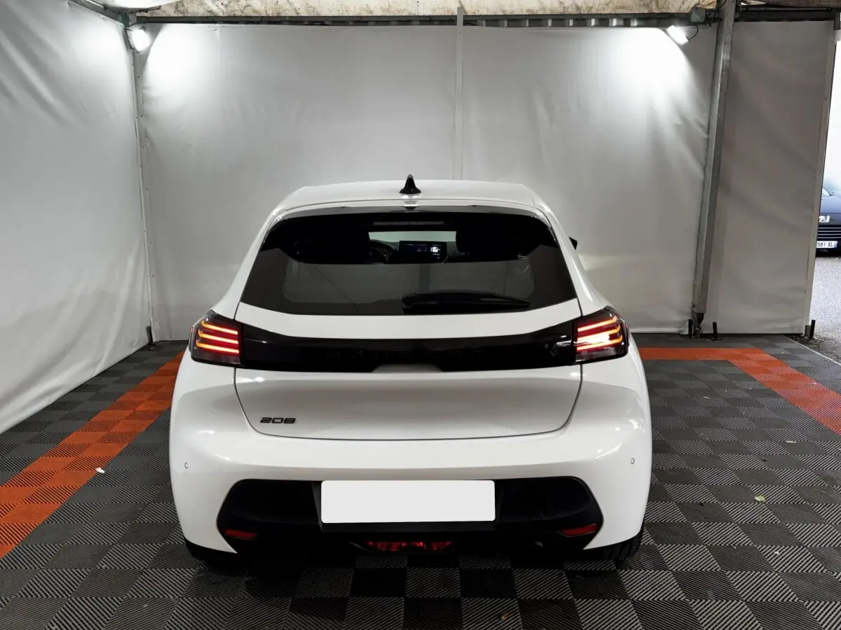 Vue arrière d'une Peugeot 208 blanche 2024 avec feux arrière LED allumés dans un espace fermé.