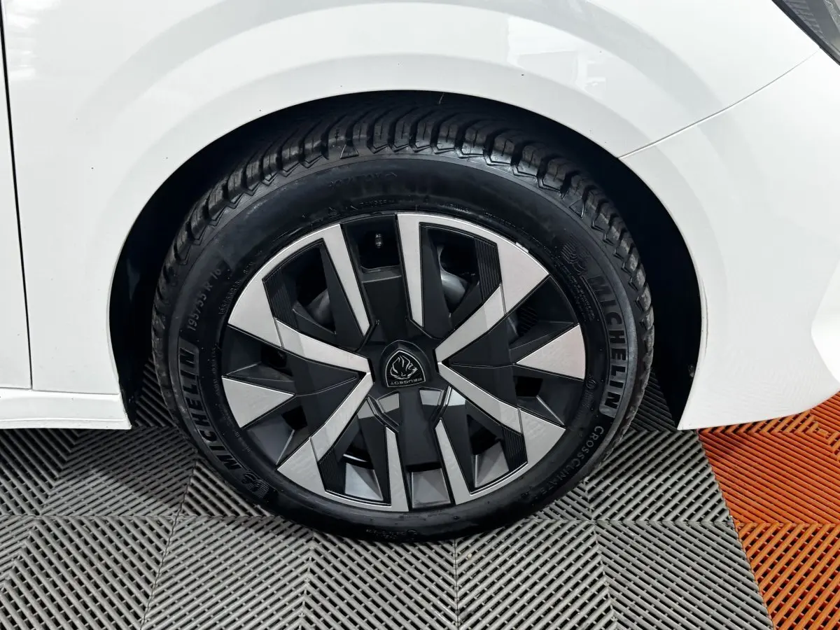 Gros plan sur la roue arrière droite d'une Peugeot 208 blanche avec jante au design géométrique bicolore.