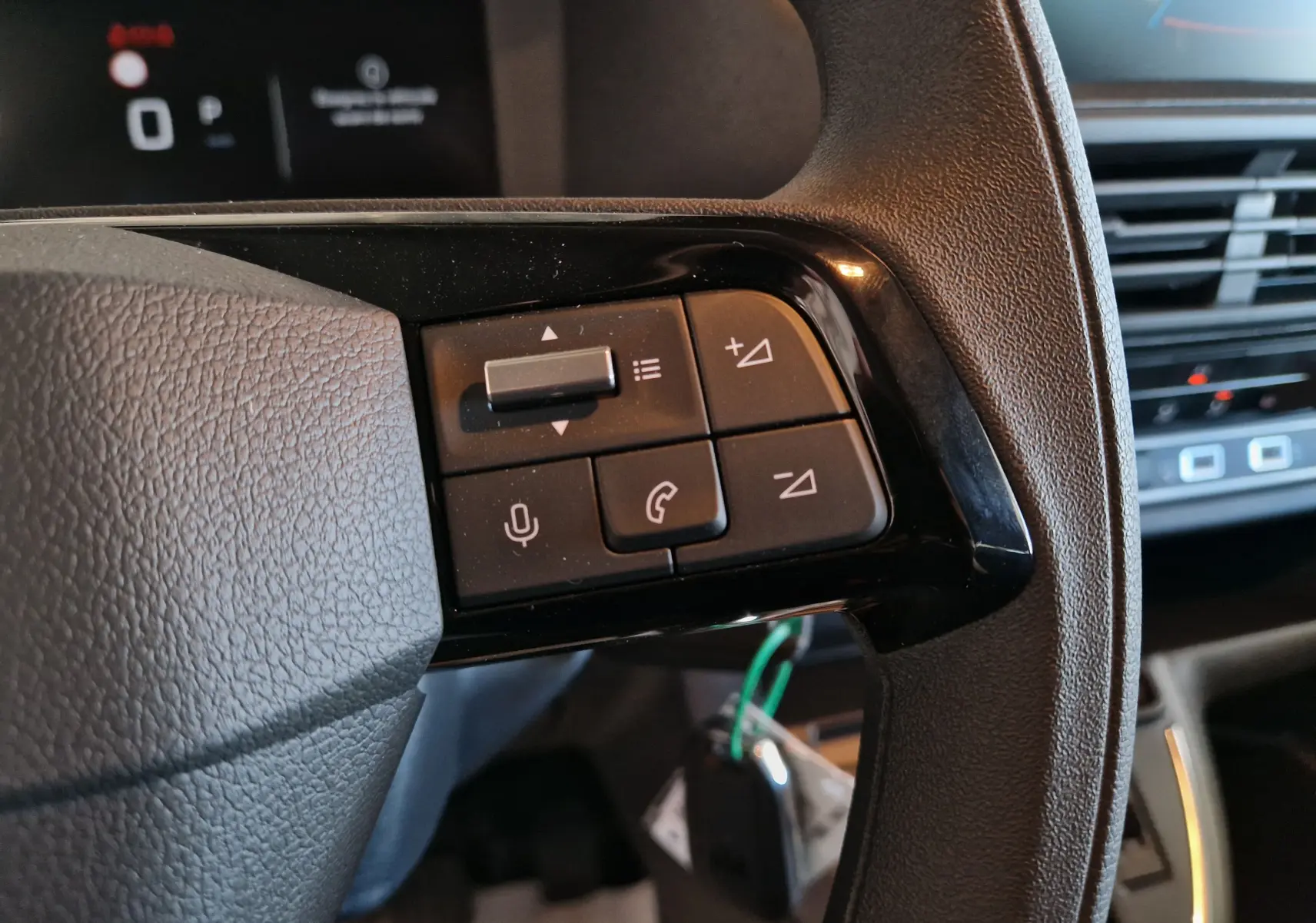 Gros plan sur les commandes du volant côté gauche du Peugeot Expert XL gris titane, avec tableau de bord numérique en arrière-plan.