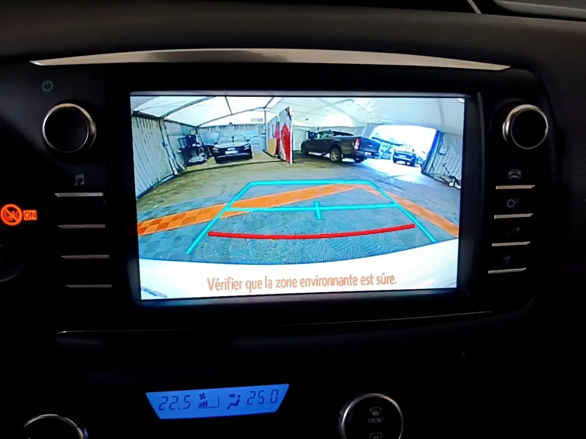 Écran tactile intérieur affichant la caméra de recul d'une Toyota Yaris blanche, avec repères de stationnement colorés.