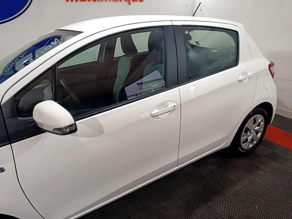 Vue latérale côté gauche d'une Toyota Yaris blanche 5 portes, avec rétroviseur blanc et jantes compactes.