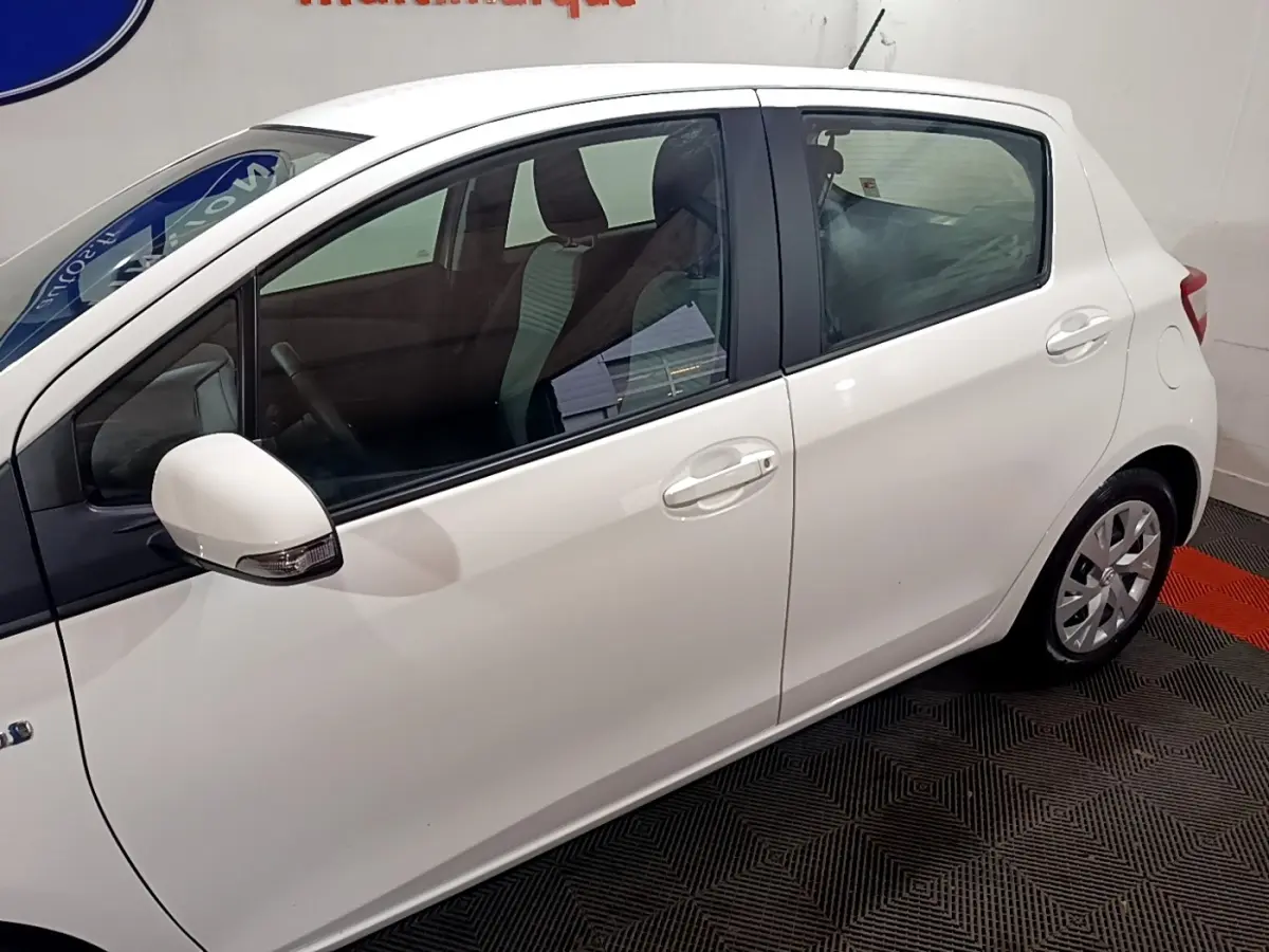Profil côté gauche d'une Toyota Yaris blanche hybride 2019, avec rétroviseur blanc et jantes alliage visibles.