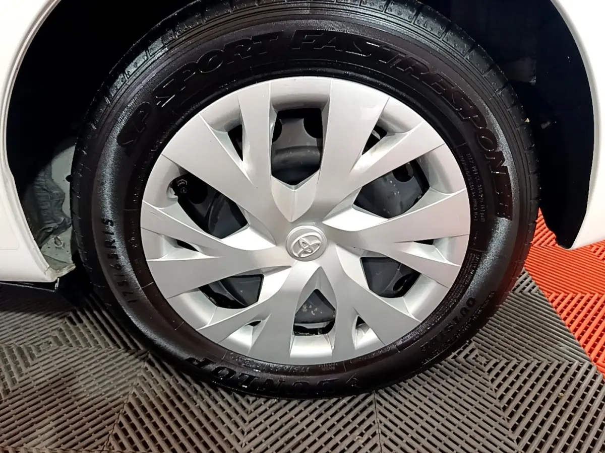 Gros plan sur la roue avant droite blanche d'une Toyota Yaris 1.5 VVT-I Hybrid France Business 2019 avec enjoliveur argenté.