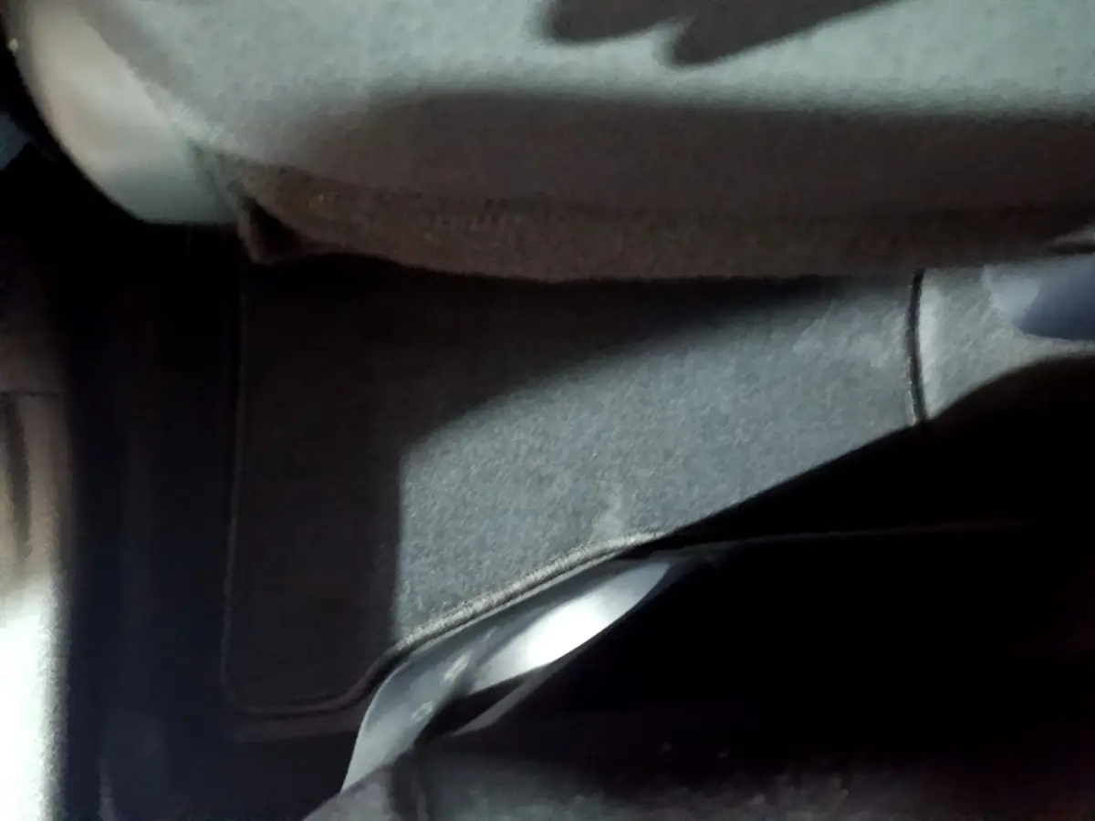 Gros plan sur le tapis de sol gris foncé sous le siège avant d'une Toyota Yaris blanche hybride 2019.