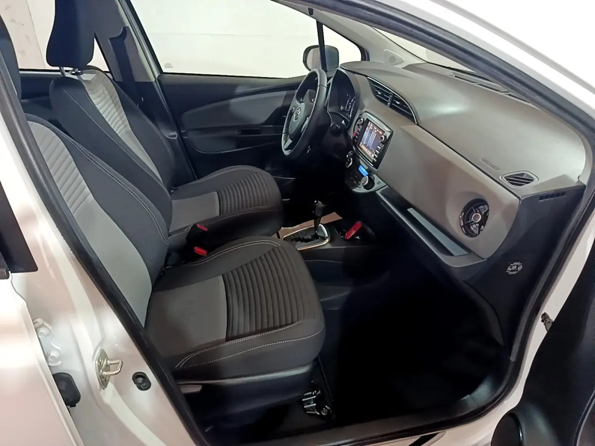 Intérieur côté conducteur d'une Toyota Yaris blanche 2019, avec sièges tissu noir et gris et tableau de bord moderne.