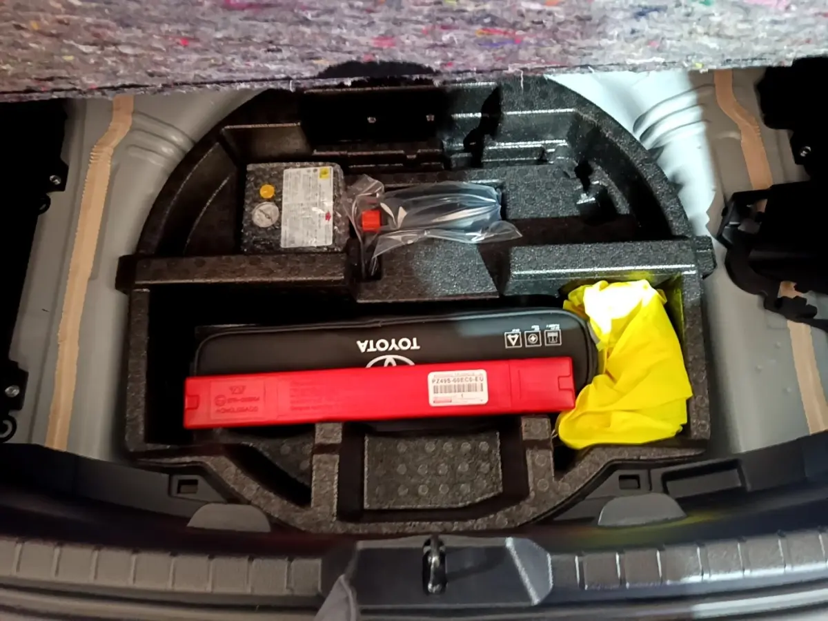 Vue plongeante sur le coffre ouvert d'une Toyota Yaris blanche, montrant le rangement avec kit de sécurité et triangle rouge.