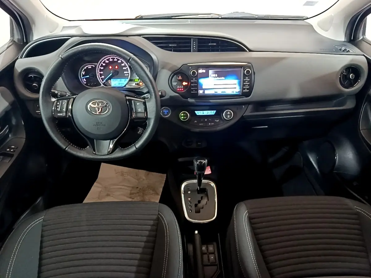 Vue intérieure frontale du tableau de bord et volant cuir de la Toyota Yaris hybride 2019 avec écran tactile central.