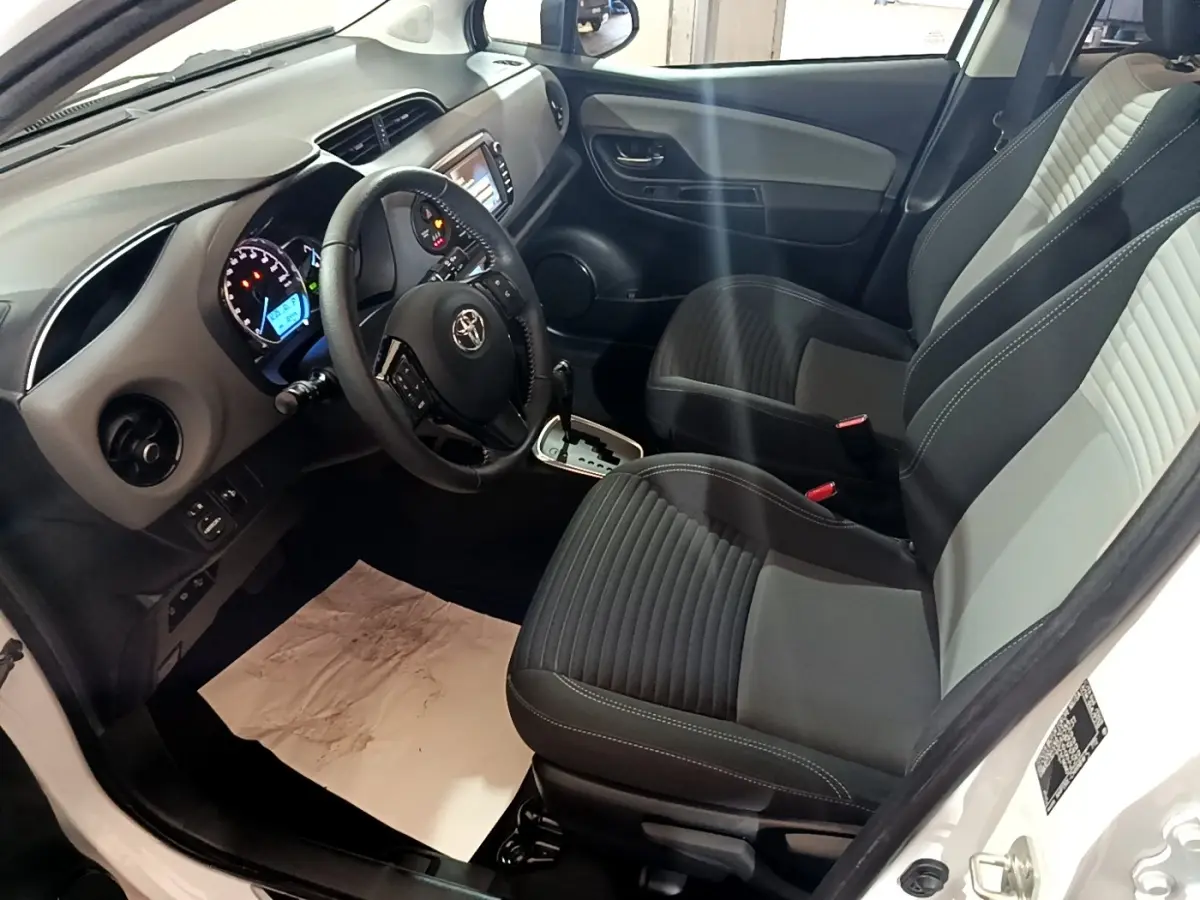 Intérieur avant droit de Toyota Yaris blanc 2019, sièges bicolores, volant cuir multifonctions et tableau de bord digital.