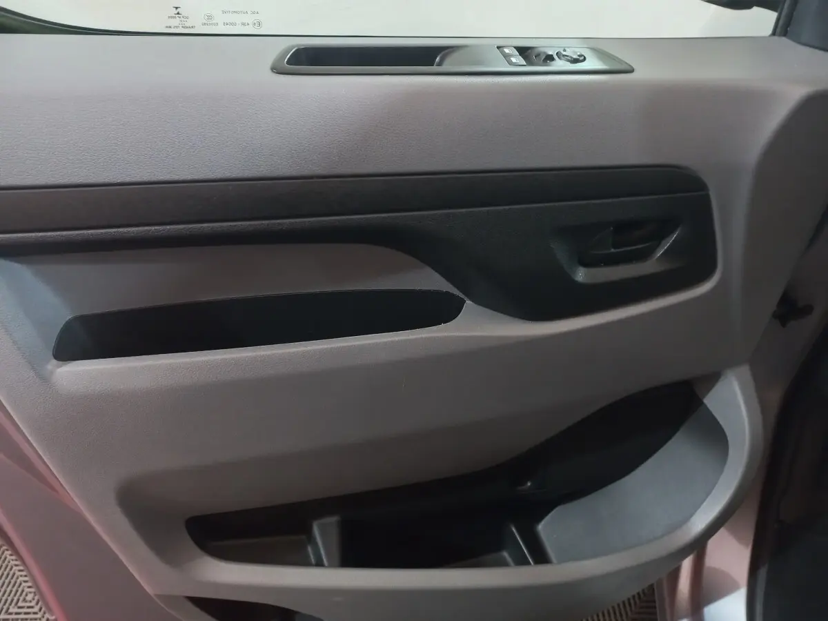 Détail de la porte intérieure côté conducteur du Peugeot Traveller gris clair, avec commandes des vitres et poignée noire.