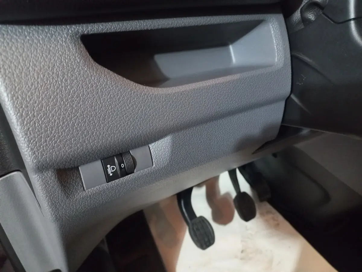 Gros plan sur la commande de réglage des phares et les pédales côté conducteur du Peugeot Traveller gris clair 2021.