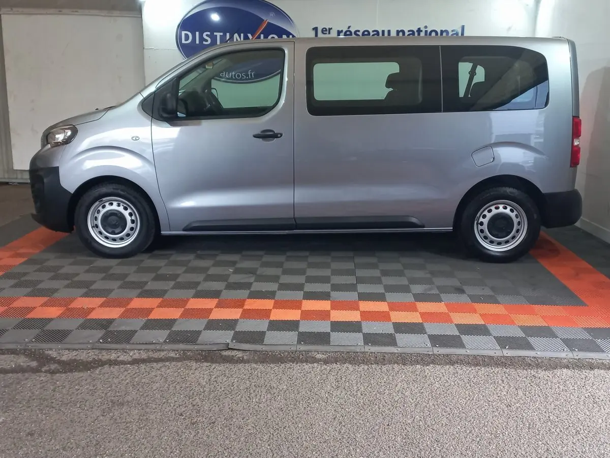 Vue latérale droite d'un Peugeot Traveller gris clair 2021 avec vitres arrière teintées et jantes acier simples.