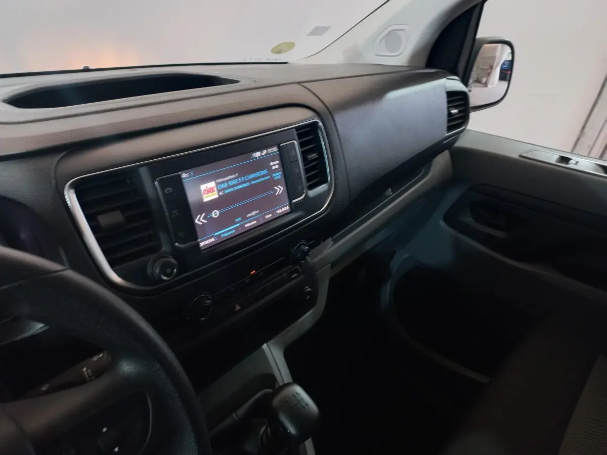 Vue intérieure côté passager du tableau de bord noir du Peugeot Traveller gris clair avec écran tactile central allumé.