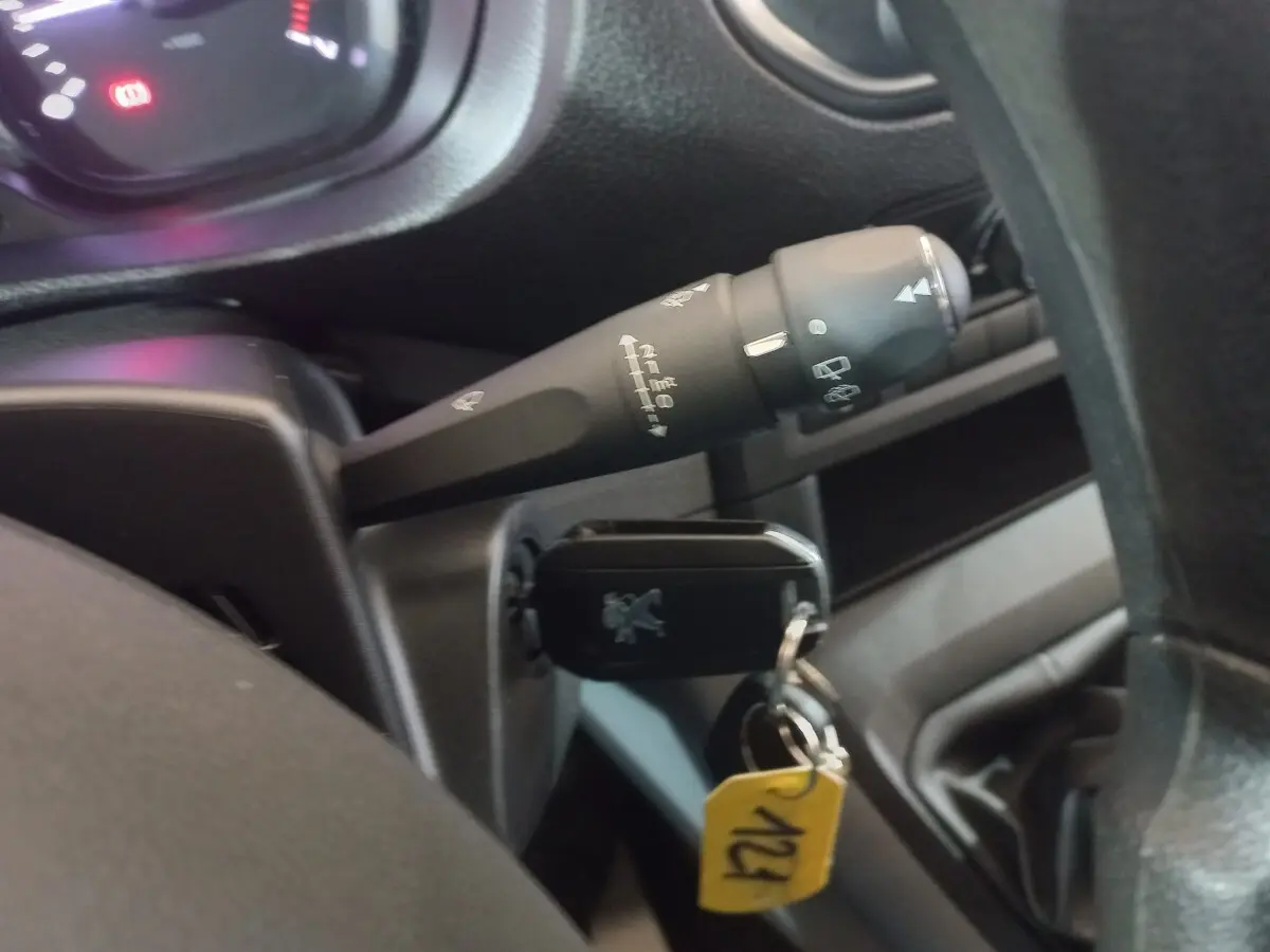 Gros plan sur la clé insérée dans le contacteur du Peugeot Traveller gris clair, avec commande d’essuie-glace visible derrière le volant.