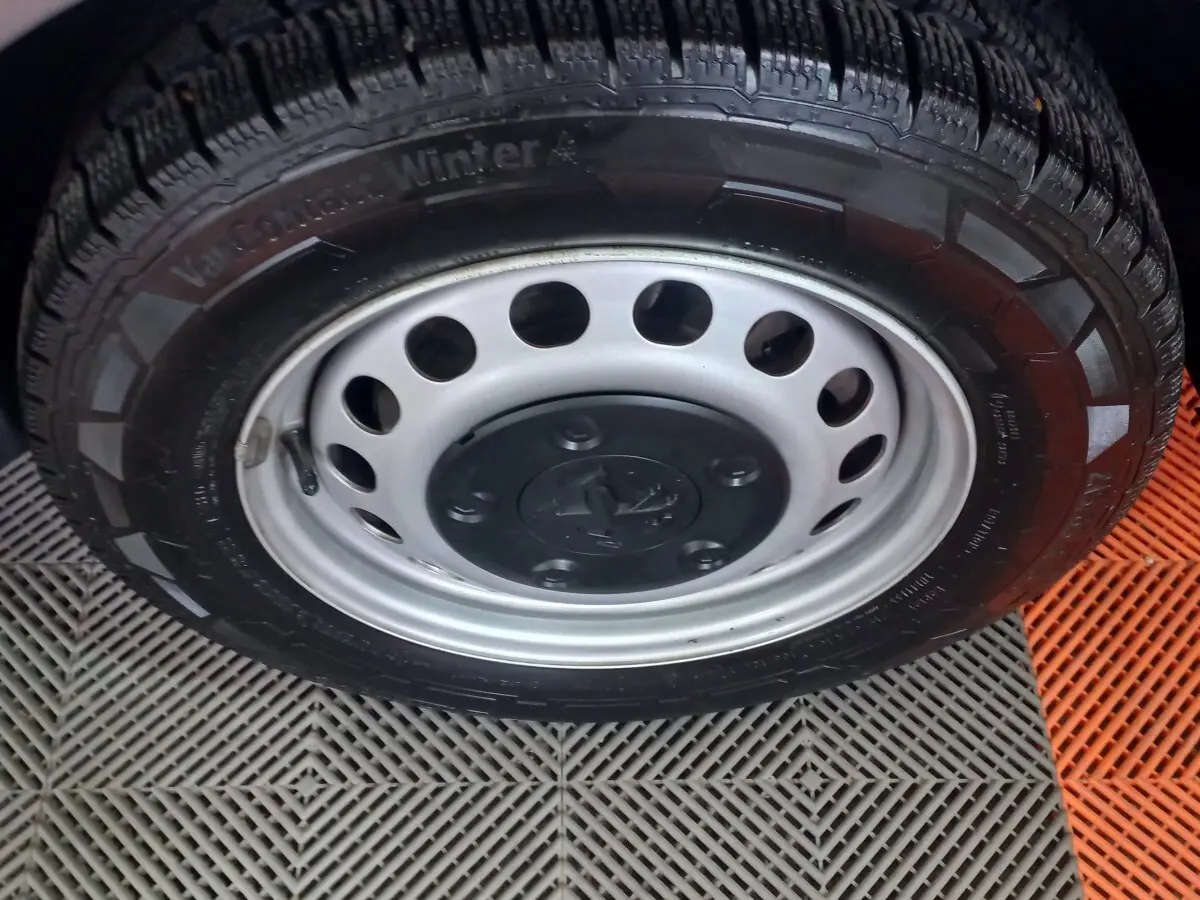 Gros plan sur la roue avant avec jante acier grise et pneu hiver du Peugeot Traveller gris clair 2021.