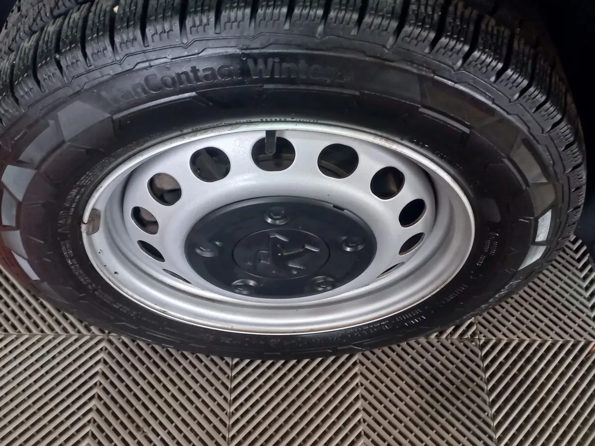 Gros plan sur la roue acier avec logo Peugeot d’un Peugeot Traveller gris clair, vue de profil côté droit.