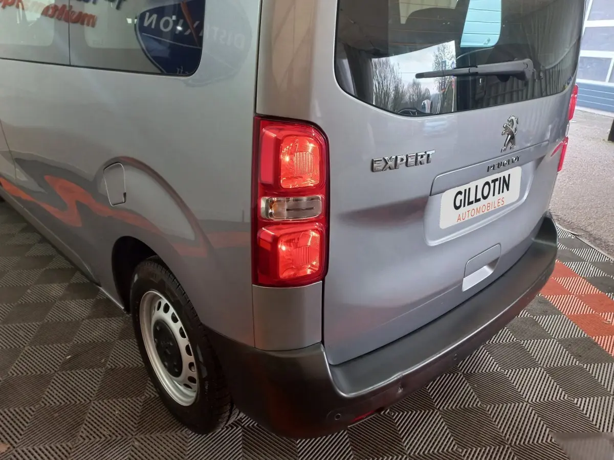 Vue 3/4 arrière droite d'un Peugeot Traveller gris clair avec feux arrière et logo Expert visibles.