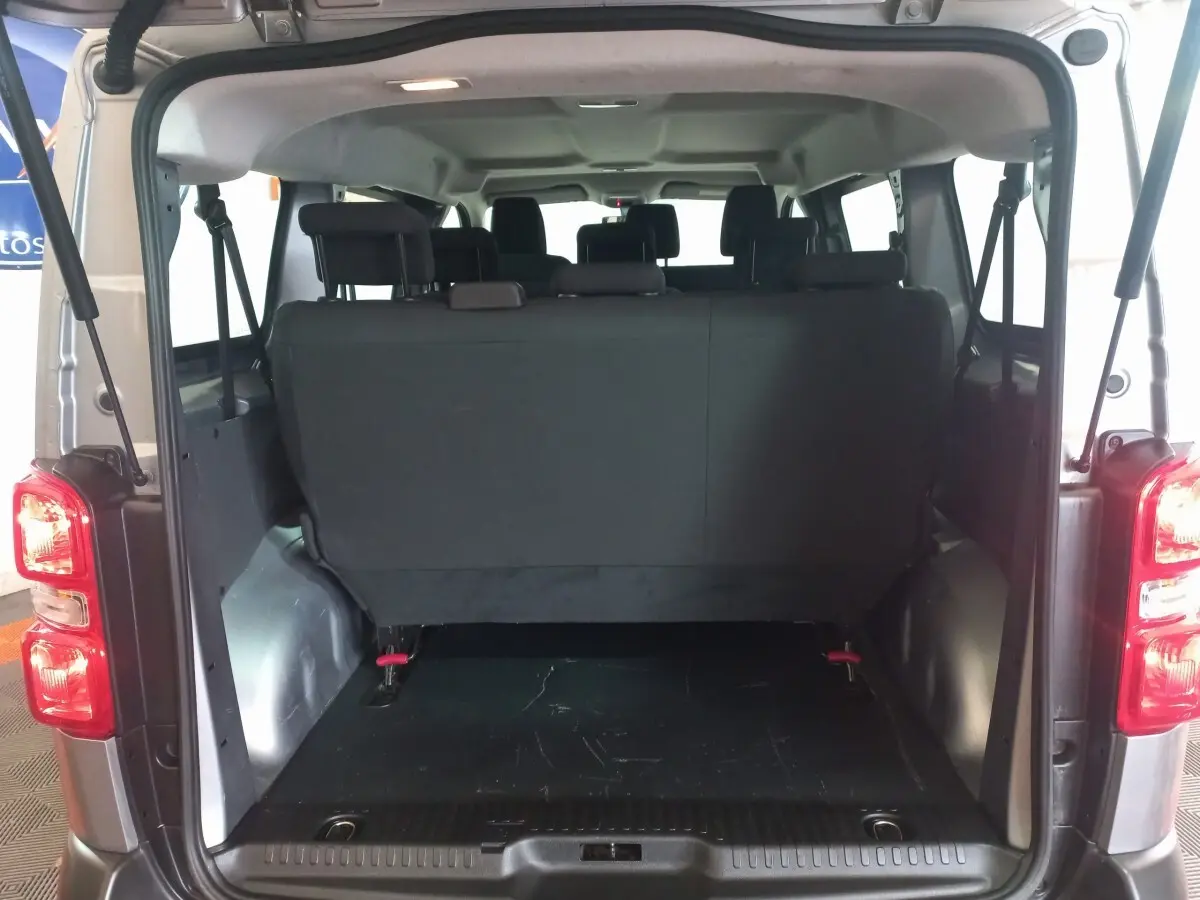 Vue arrière ouverte du Peugeot Traveller gris clair montrant la troisième rangée de sièges rabattables et l'espace de coffre.